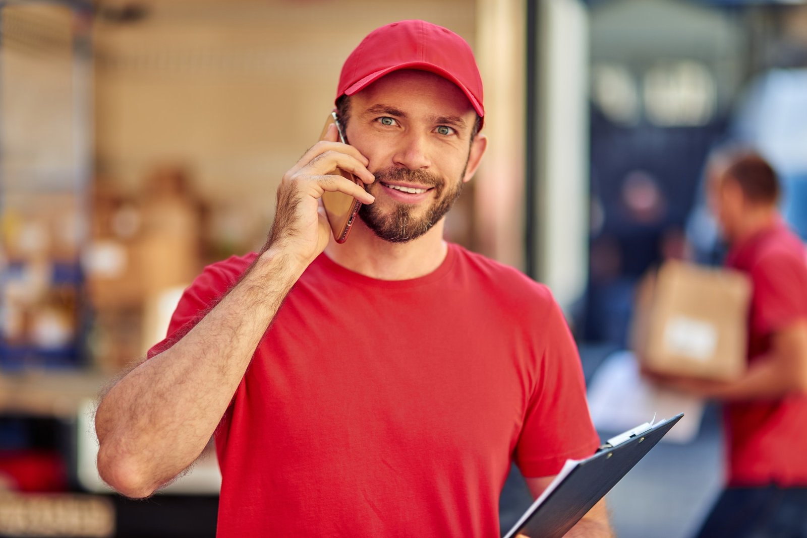 young-cheerful-caucasian-male-courier-in-red-uniform-talking-on-phone.jpg